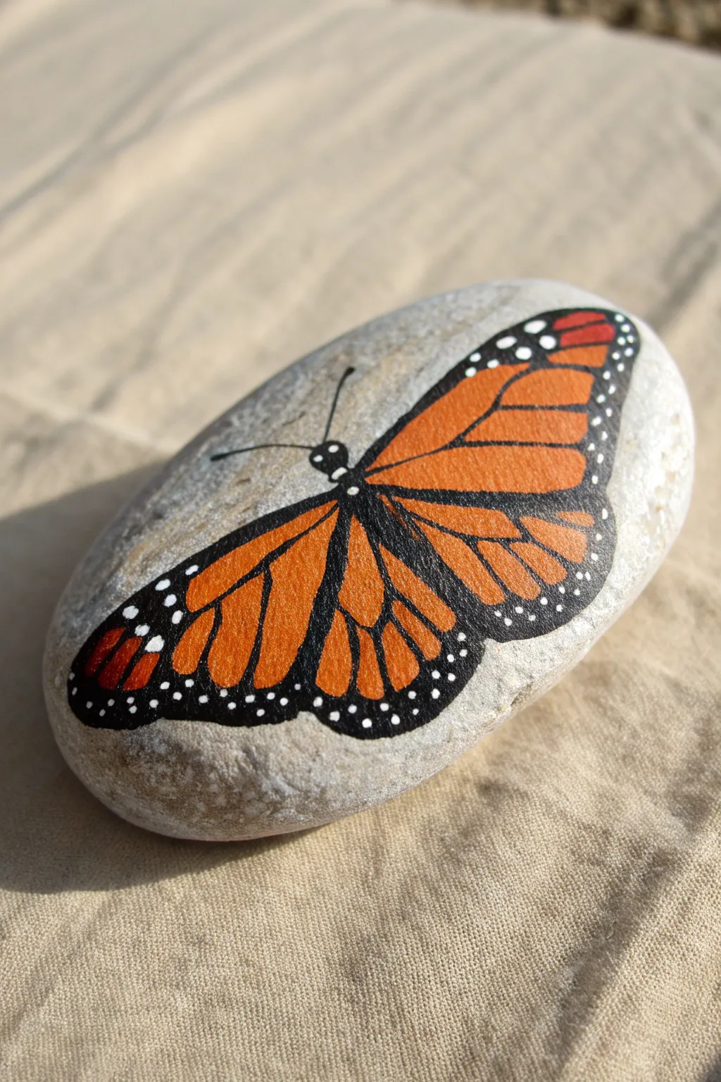 Classic monarch butterfly rock painting: bold orange wings, crisp black veins, and dotted edges.