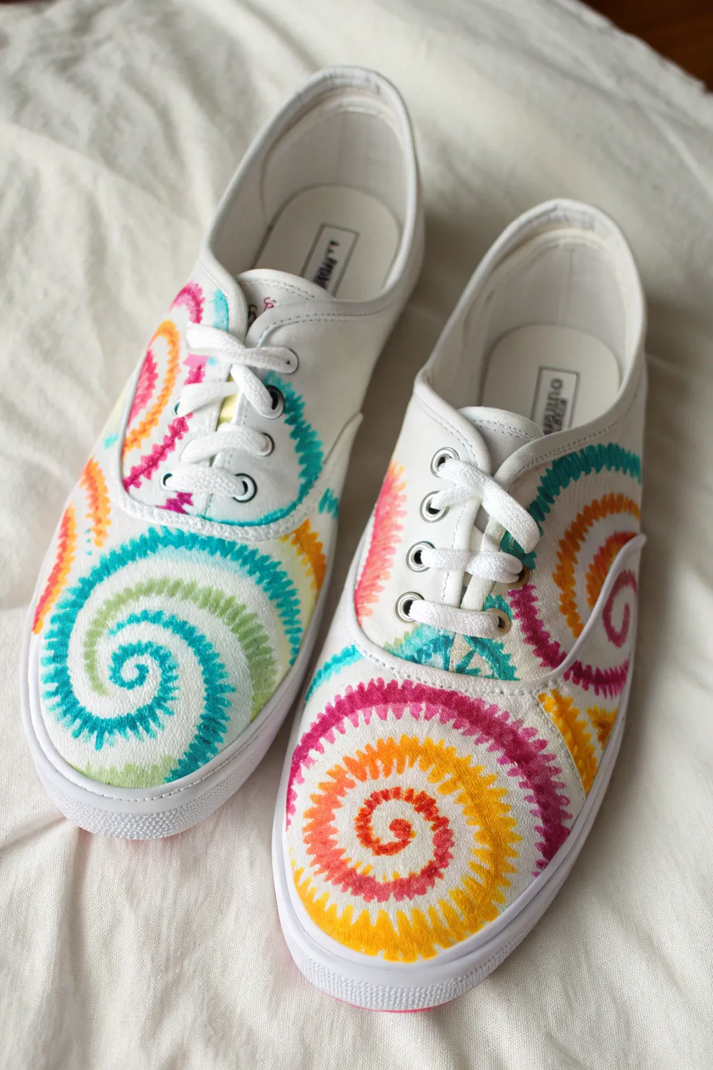 Bright spiral tie-dye swirls on crisp canvas shoes, minimalist flat lay for boho craft inspo