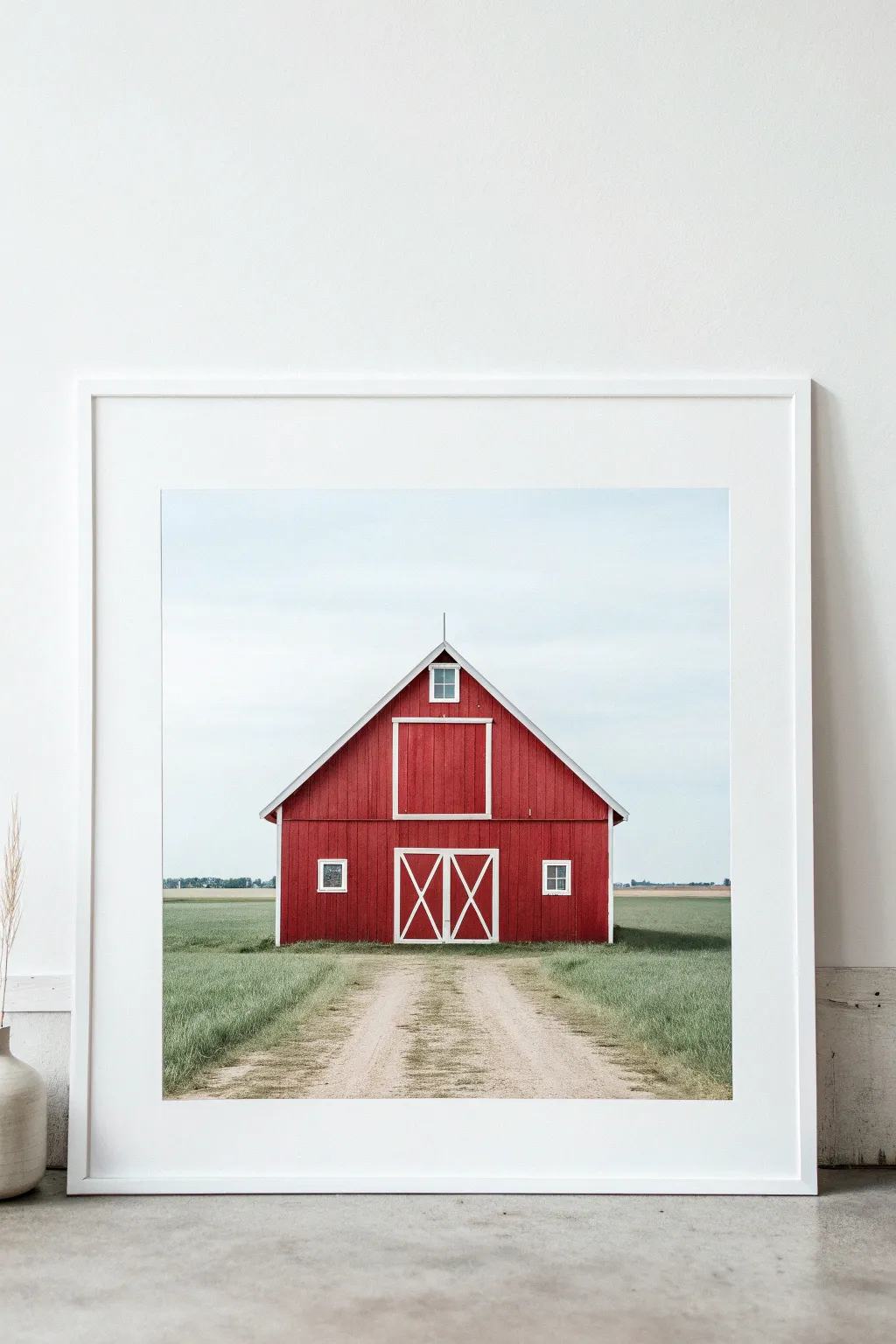 Classic red barn with white trim in simple shapes, set against a calm sky and flat field