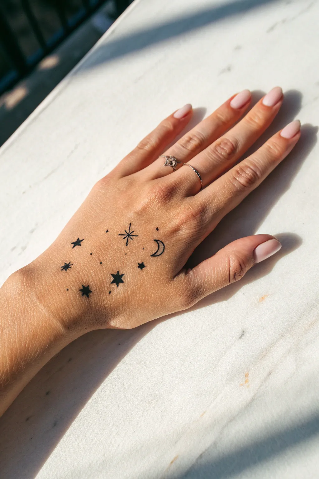 Tiny star and moon doodles across knuckles, a minimalist galaxy look in crisp black ink