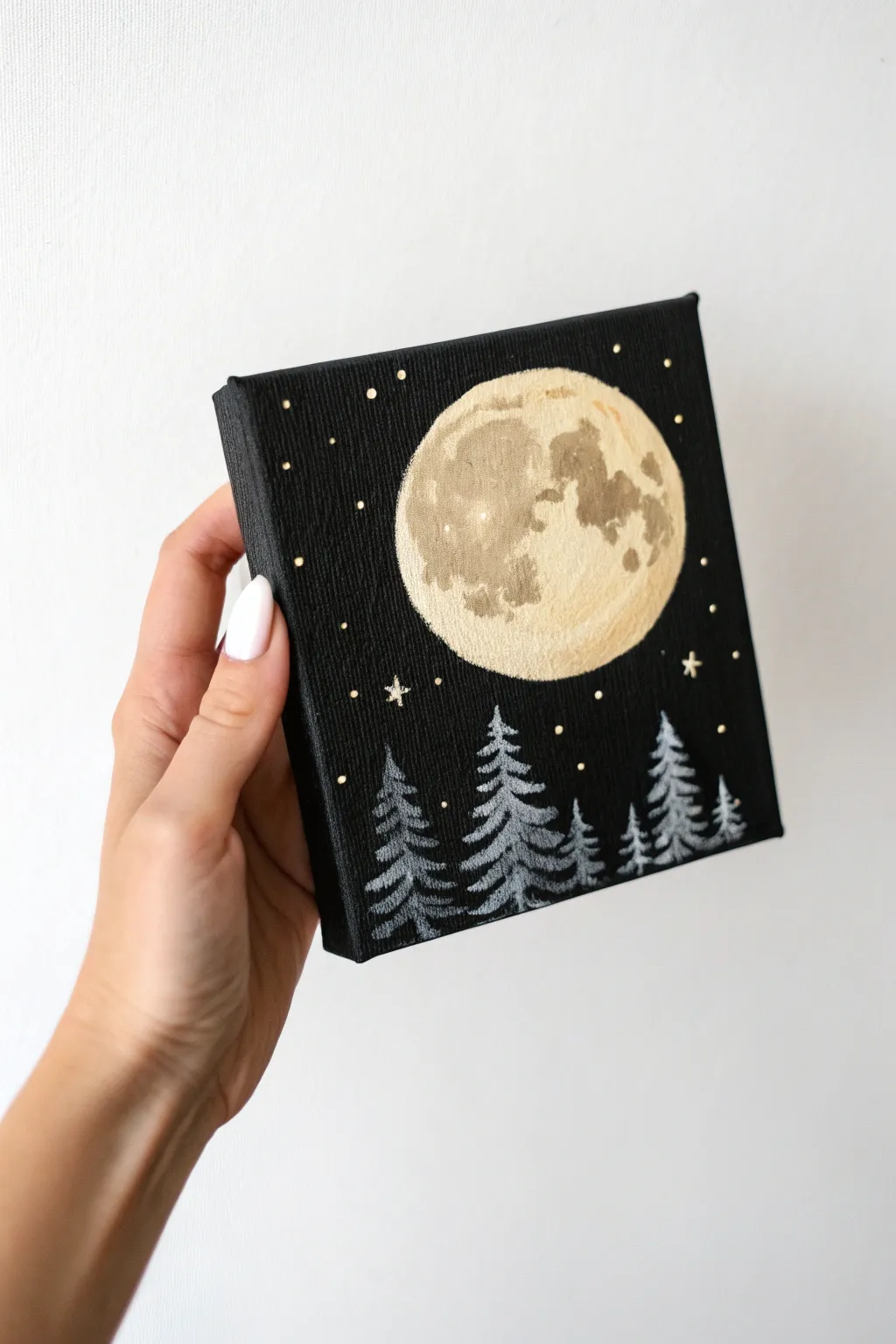 Tiny black canvas with a glowing moon and pine silhouettes, simple and calming to paint