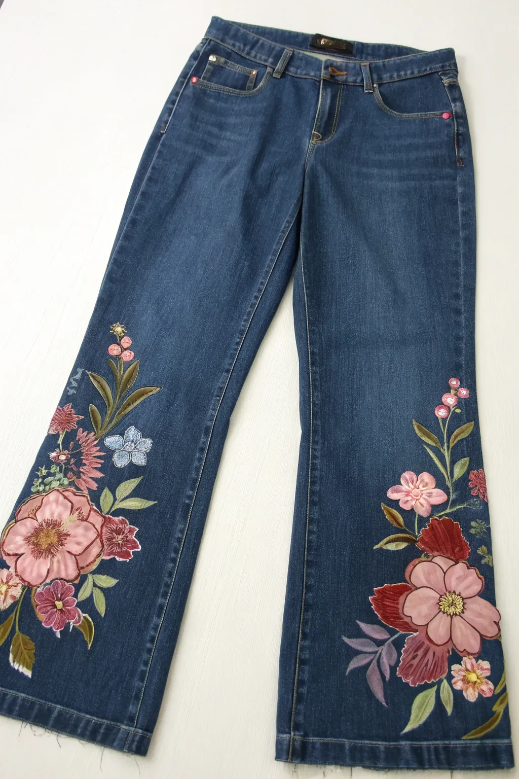 Oversized hand-painted florals climb one jean leg, crisp brushstrokes and denim texture.