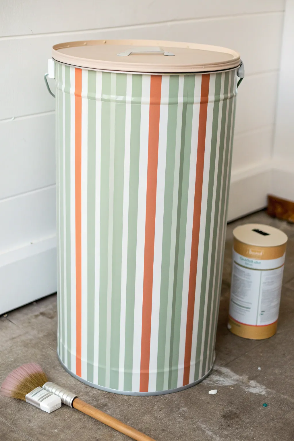 Bold striped trash can makeover with clean tape lines in calm boho hues, ready to paint.