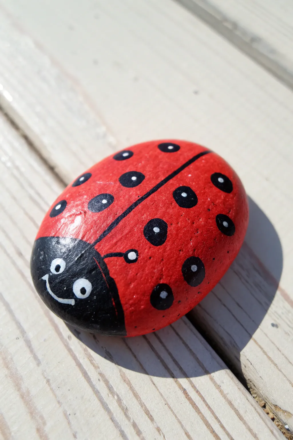 Classic ladybug rock: bright red with black dots on pale wood, minimal, handmade, and sweet.