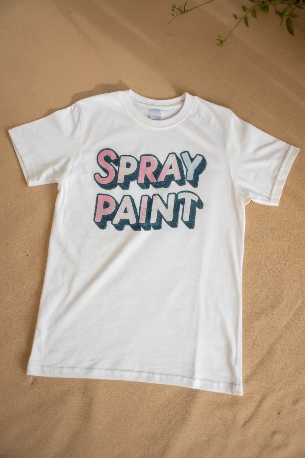 Clean flat lay of a white tee with an airbrushed graffiti name, minimalist boho DIY contrast