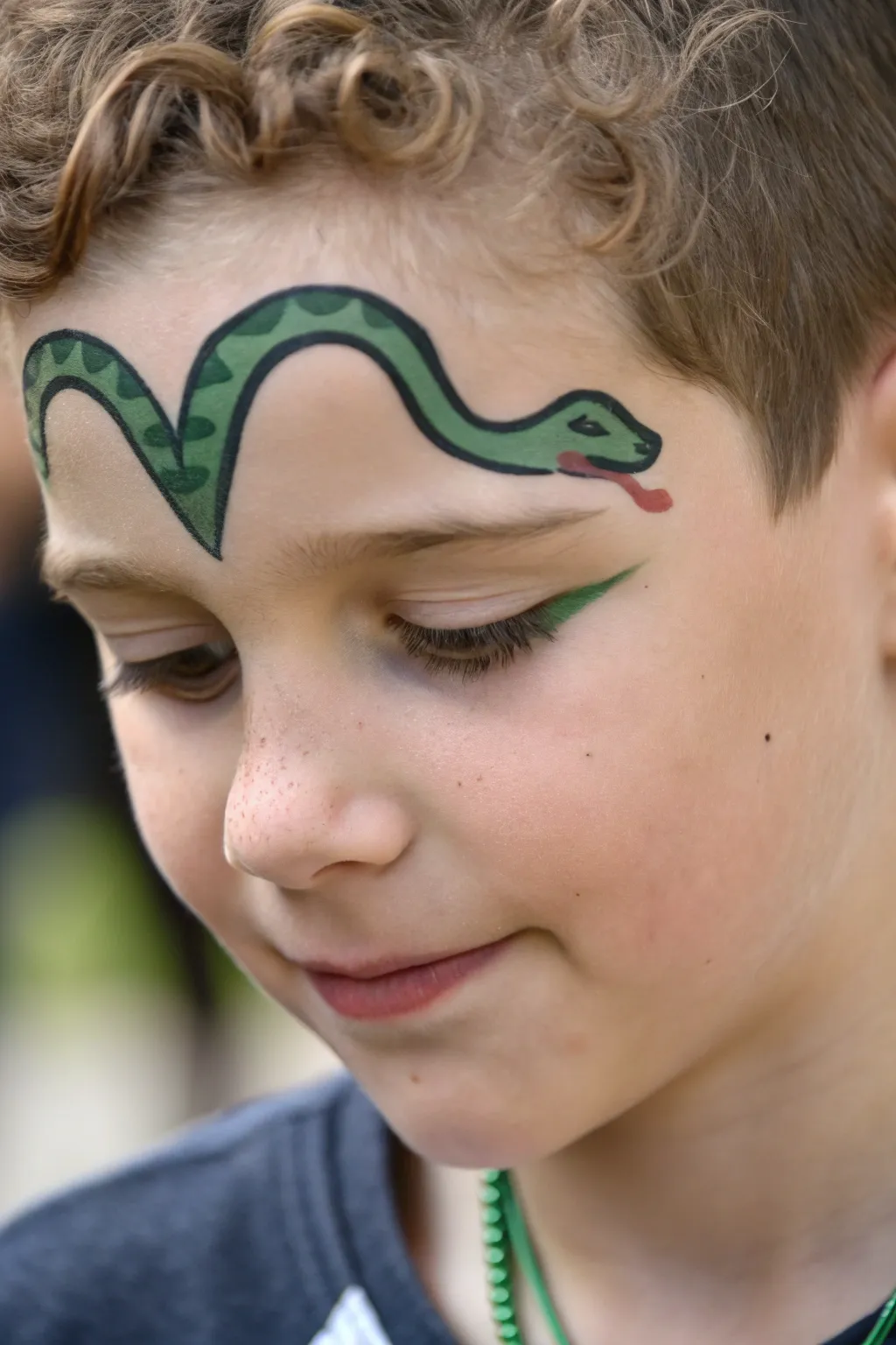 Snake wrap brow face paint for boys: clean curved lines, triangle head, and a playful forked tongue.