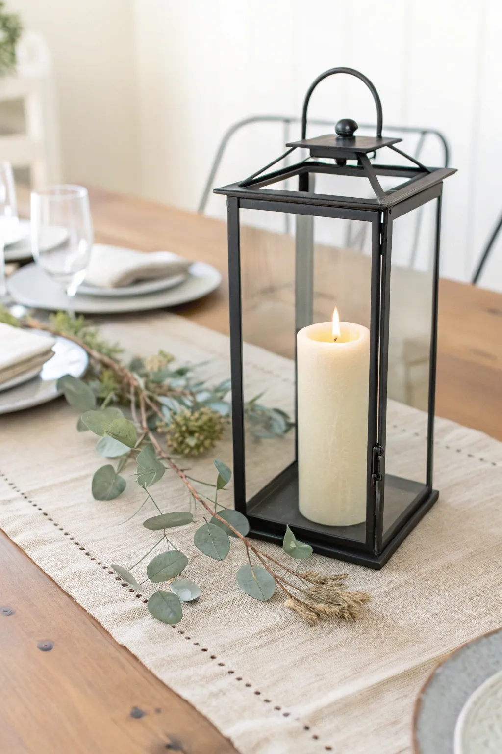 Scandi table runner centerpiece with a glowing lantern and soft dried greens for cozy minimal style.