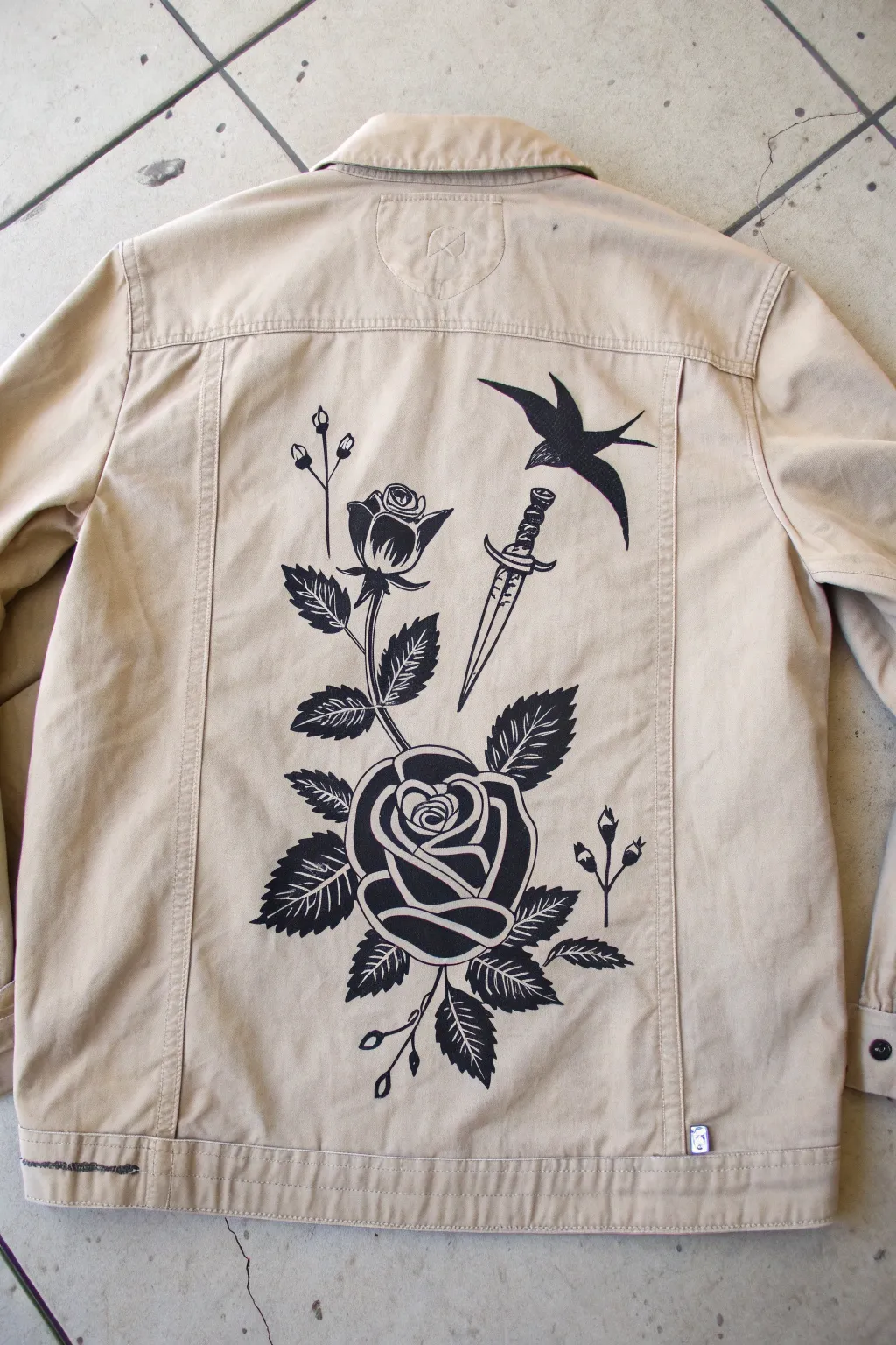 Minimal monochrome tattoo-flash jacket back art with rose, dagger, and swallow shading details