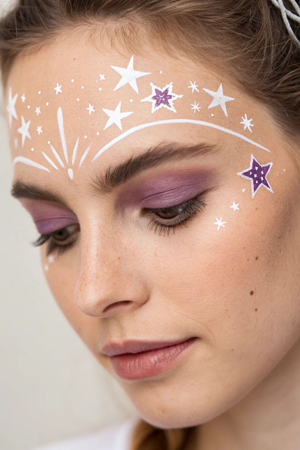Deep violet starry diadem face paint with crisp white starbursts for a minimalist princess look