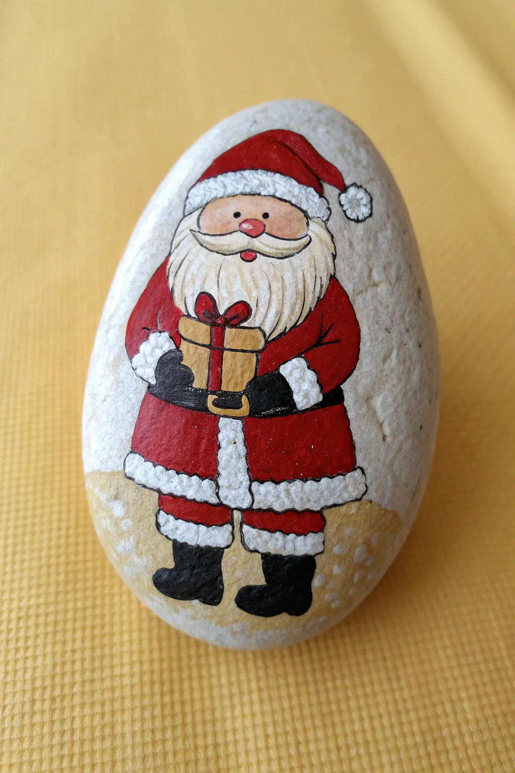 Full-body Santa rock holding a tiny present, zoomed in so the bow and ribbon details pop.