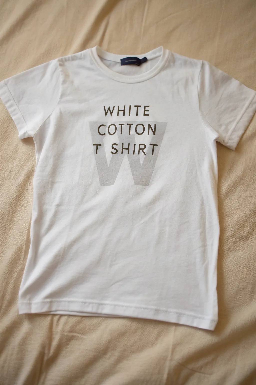 Minimalist spray-painted tee with crisp negative-space monogram cutout, clean and boho-neutral.