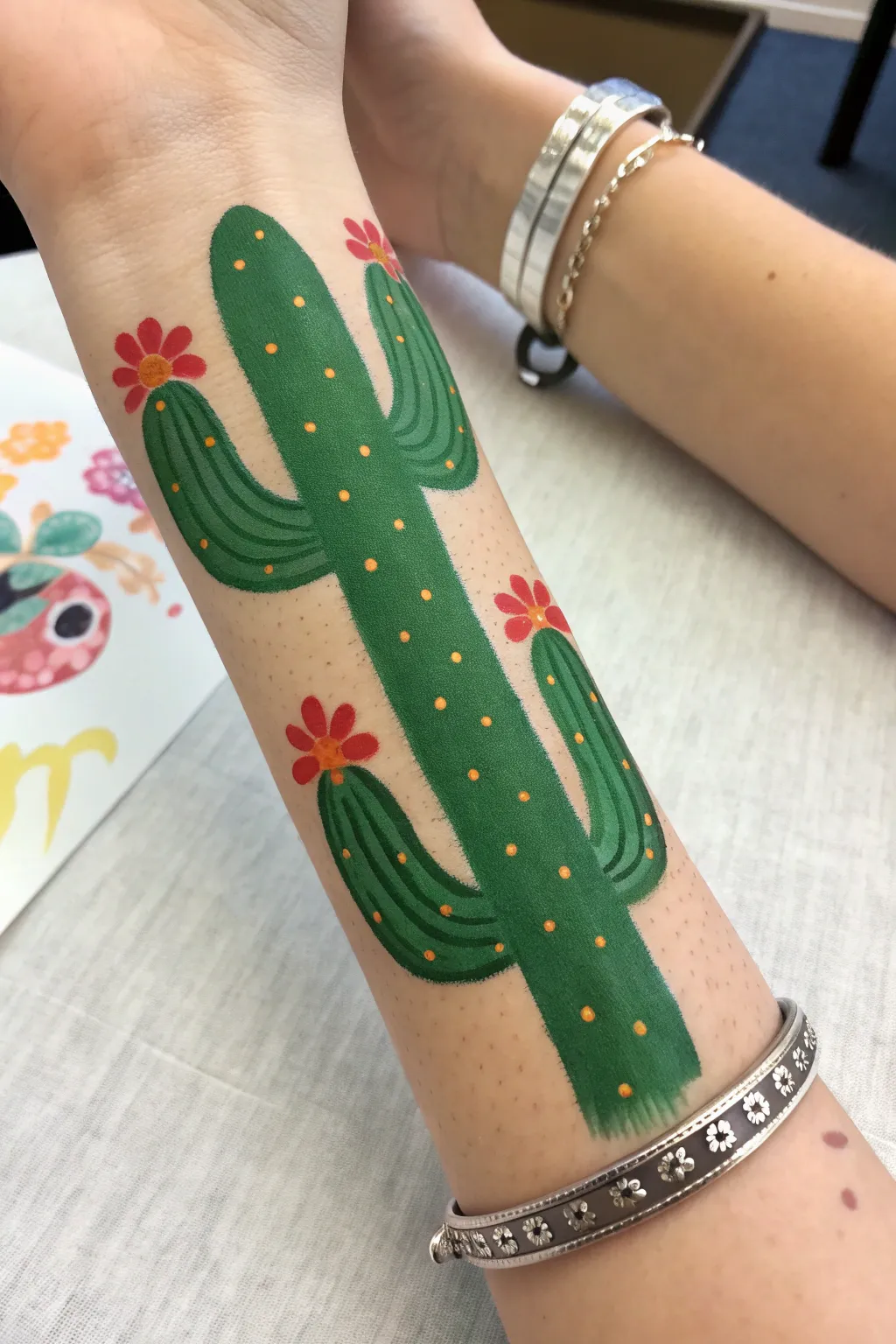 Easy arm painting idea: minimalist cactus column with tiny blooms, bold green and coral dots.