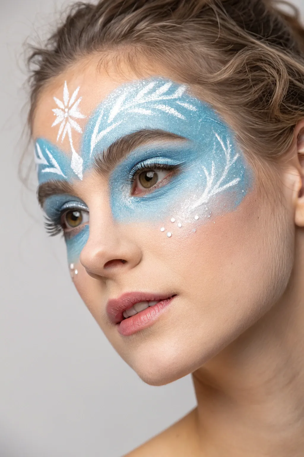 Icy blue frosted eye mask face paint with snowy highlights and delicate temple snowflakes