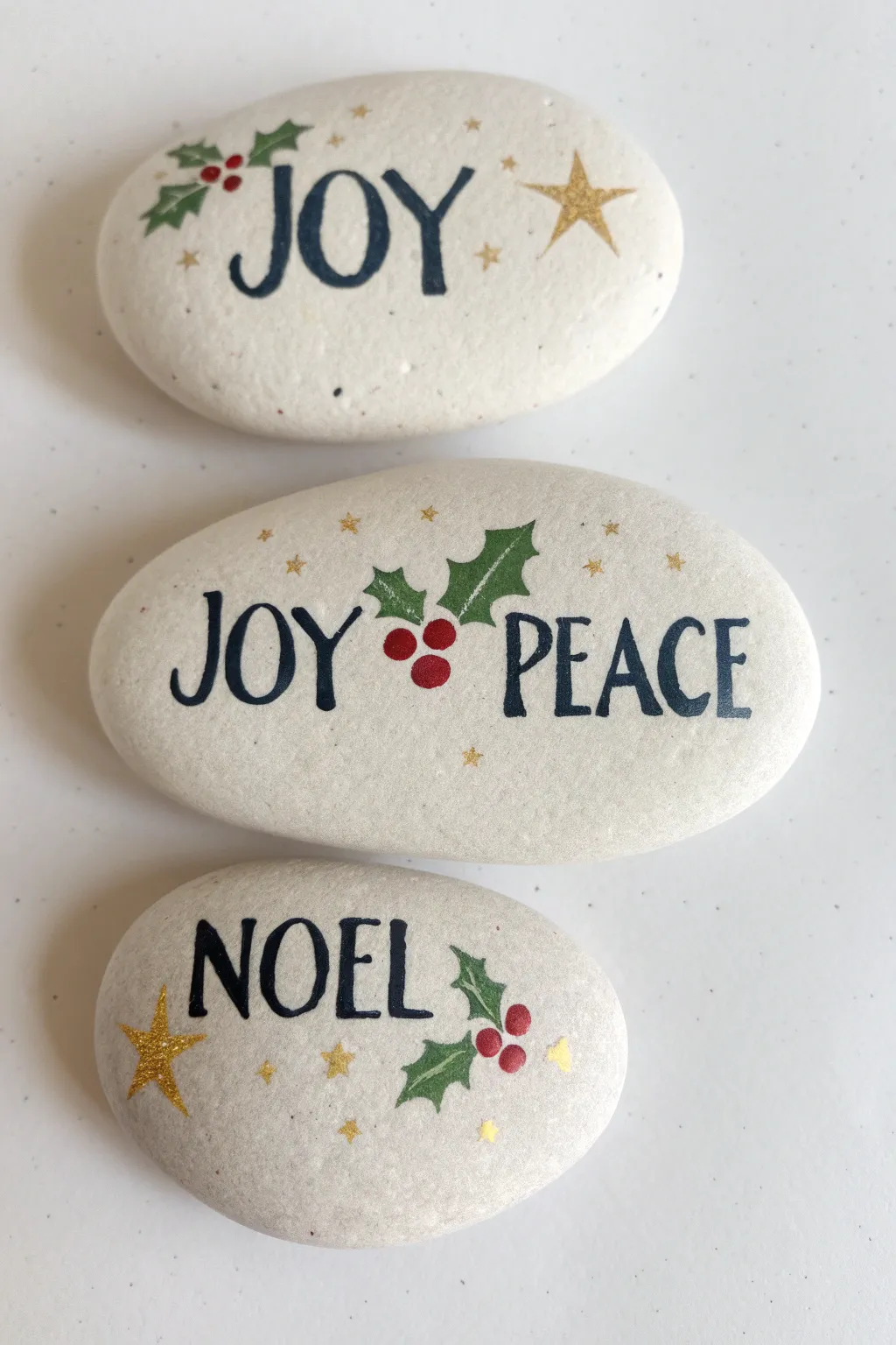 Minimalist Christmas rock painting trio with bold lettering and tiny holly accents