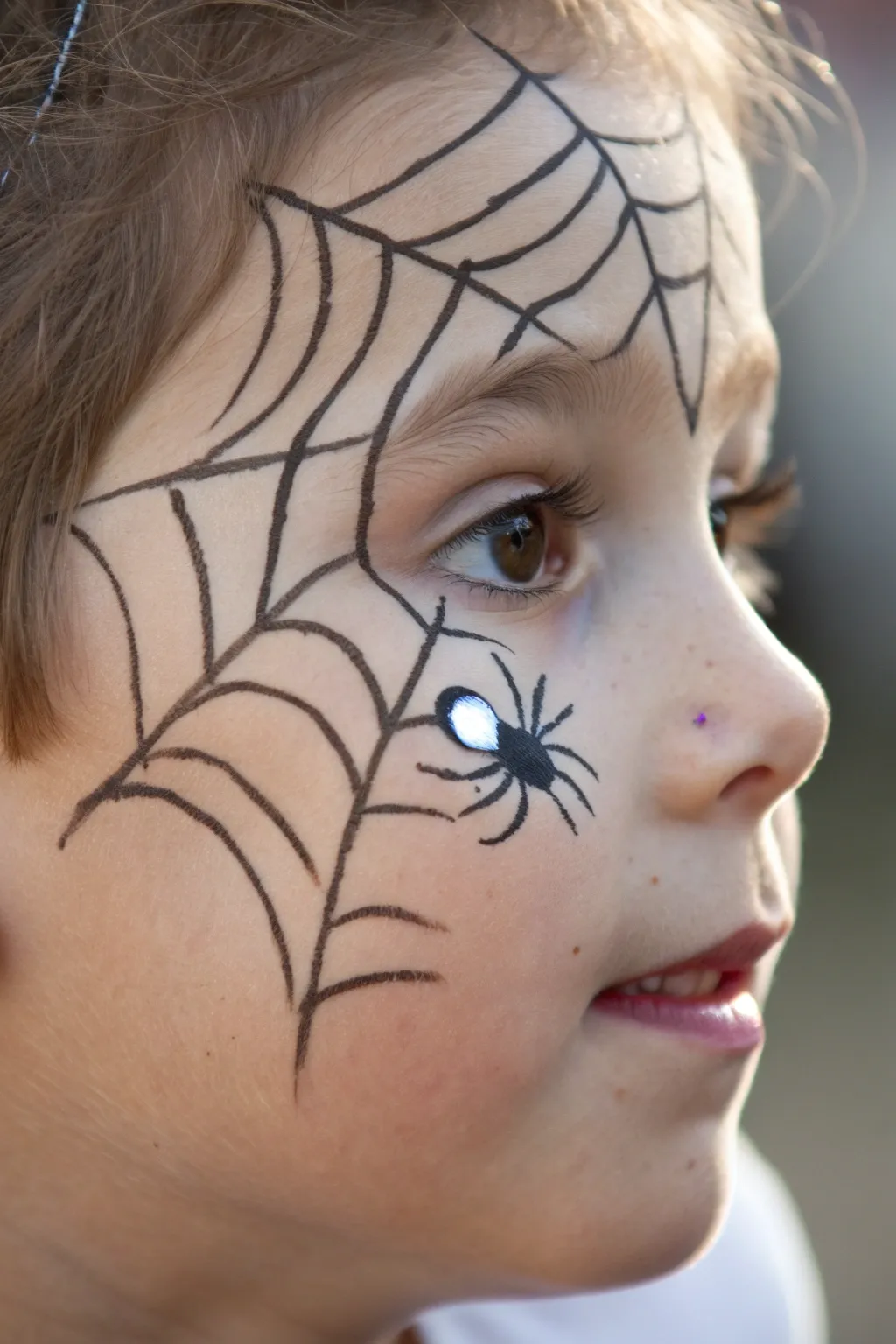 Simple spider web corner face paint for kids with bold black lines and a tiny spider detail