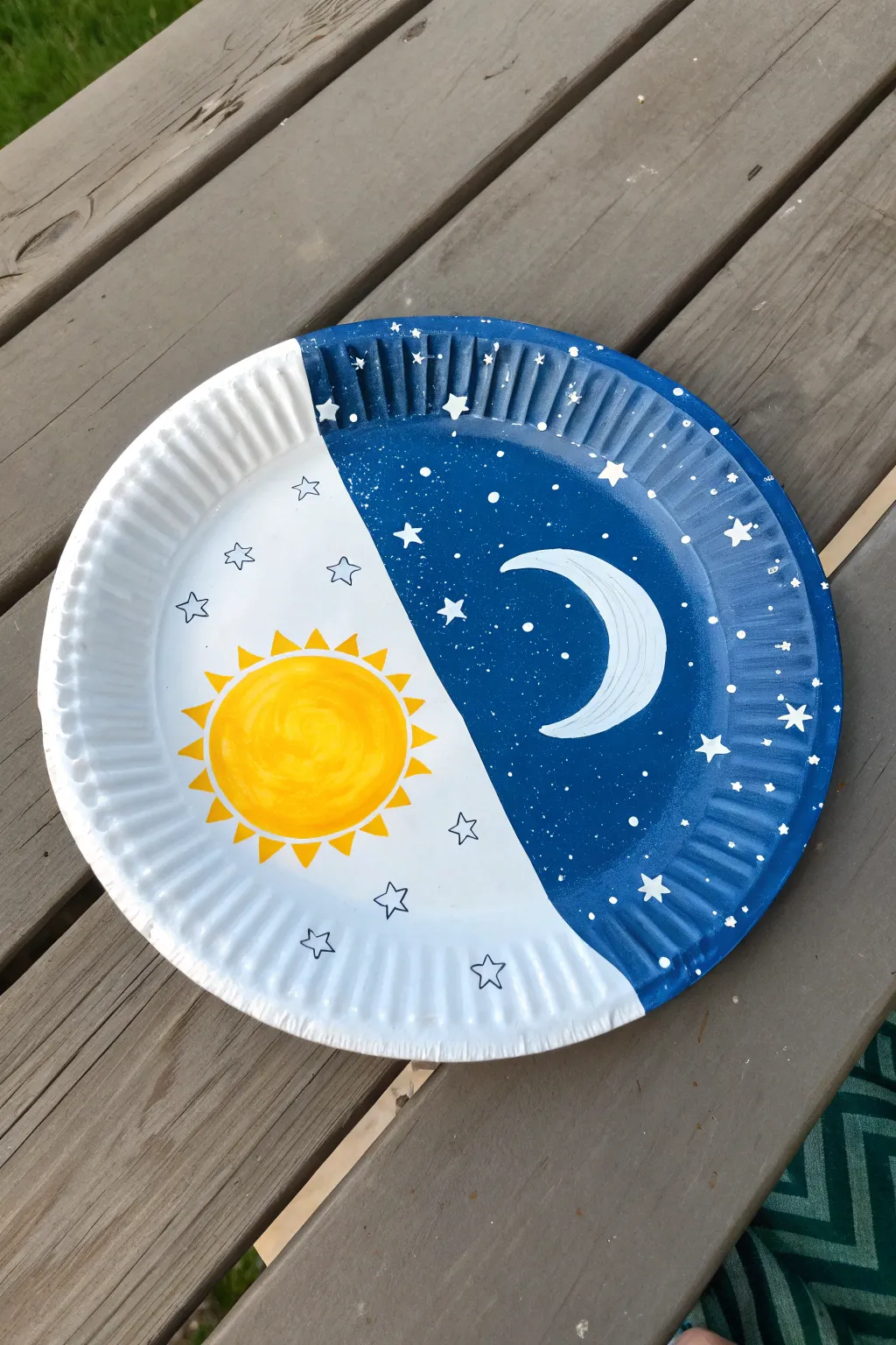Night-and-day split sky paper plate painting with sun, moon, stars and bold contrast on a clean backdrop.