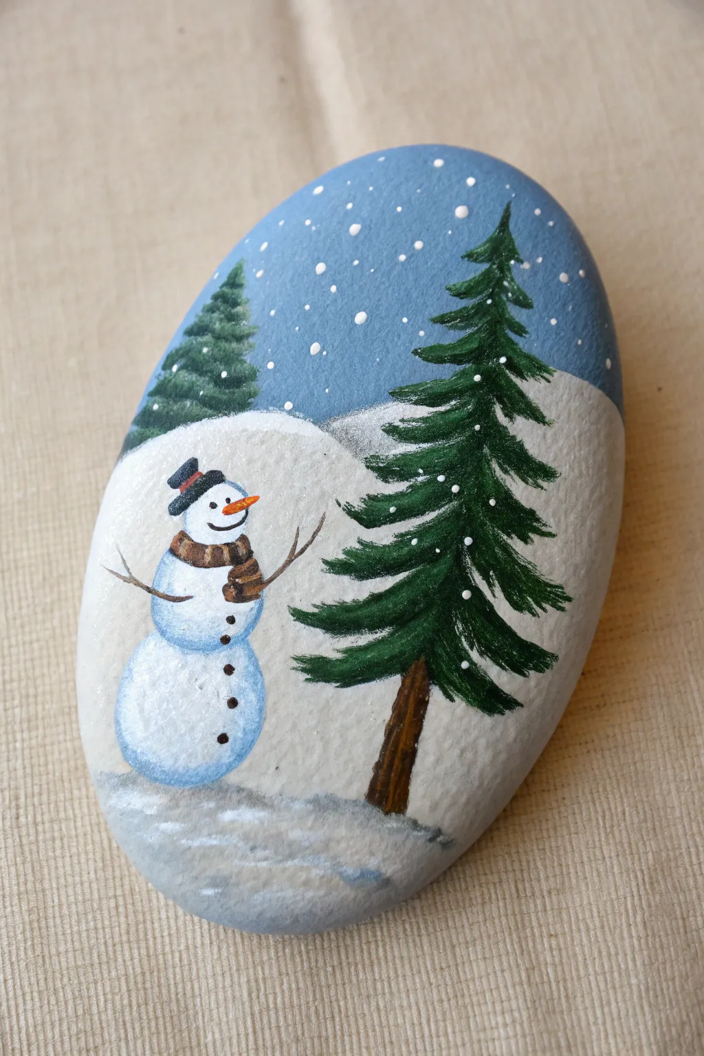 Minimal winter rock art: a snowman and pine tree on a dreamy blue sky with snowy ground.