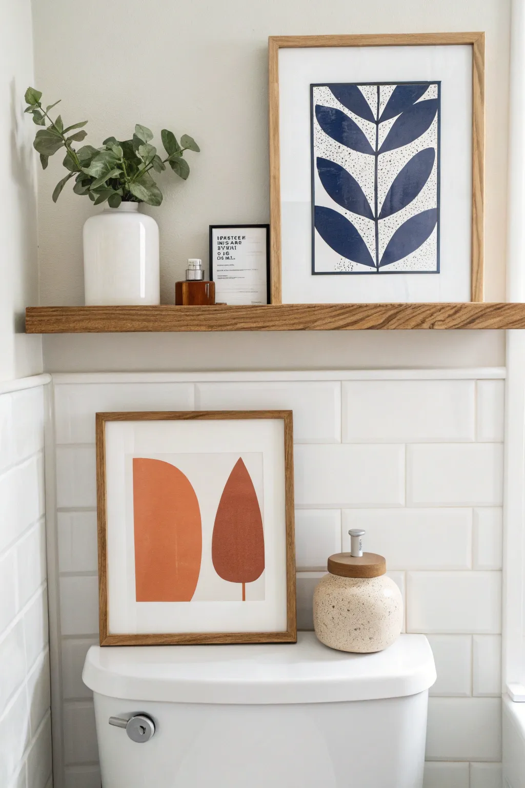 Floating shelf above the toilet with leaning frames and a tiny plant for calm, curated bathroom art