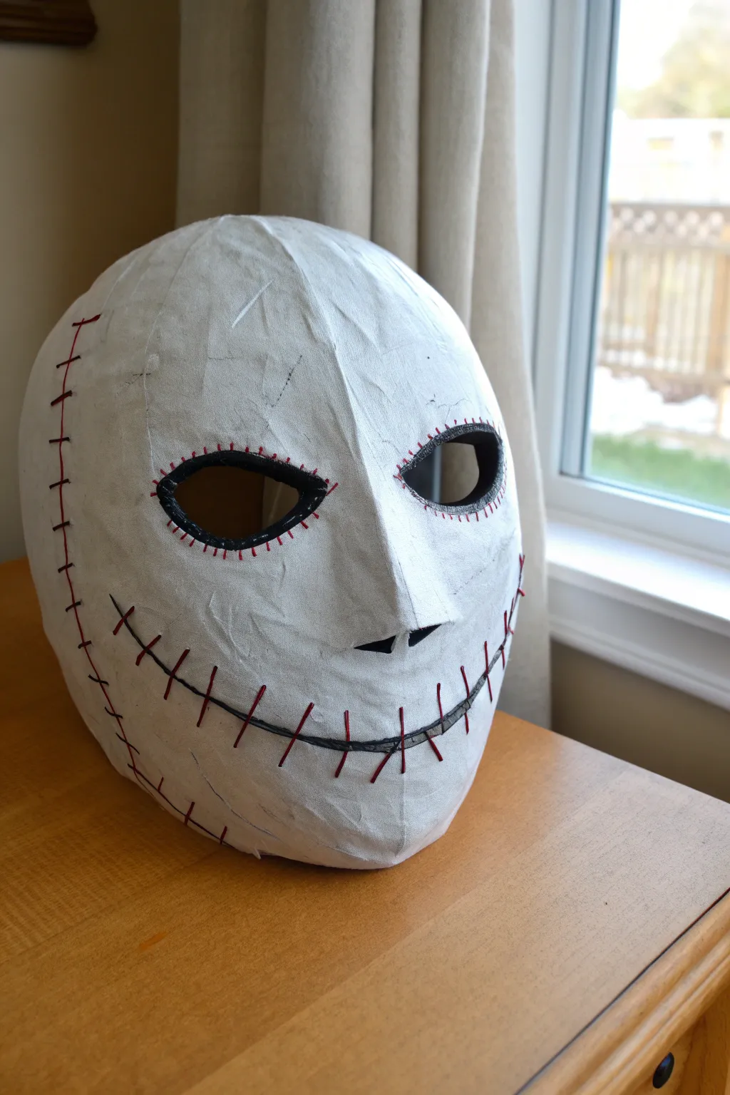 Minimal stitched-mouth Halloween mask: clean matte white base with bold cross-stitches and red shading.