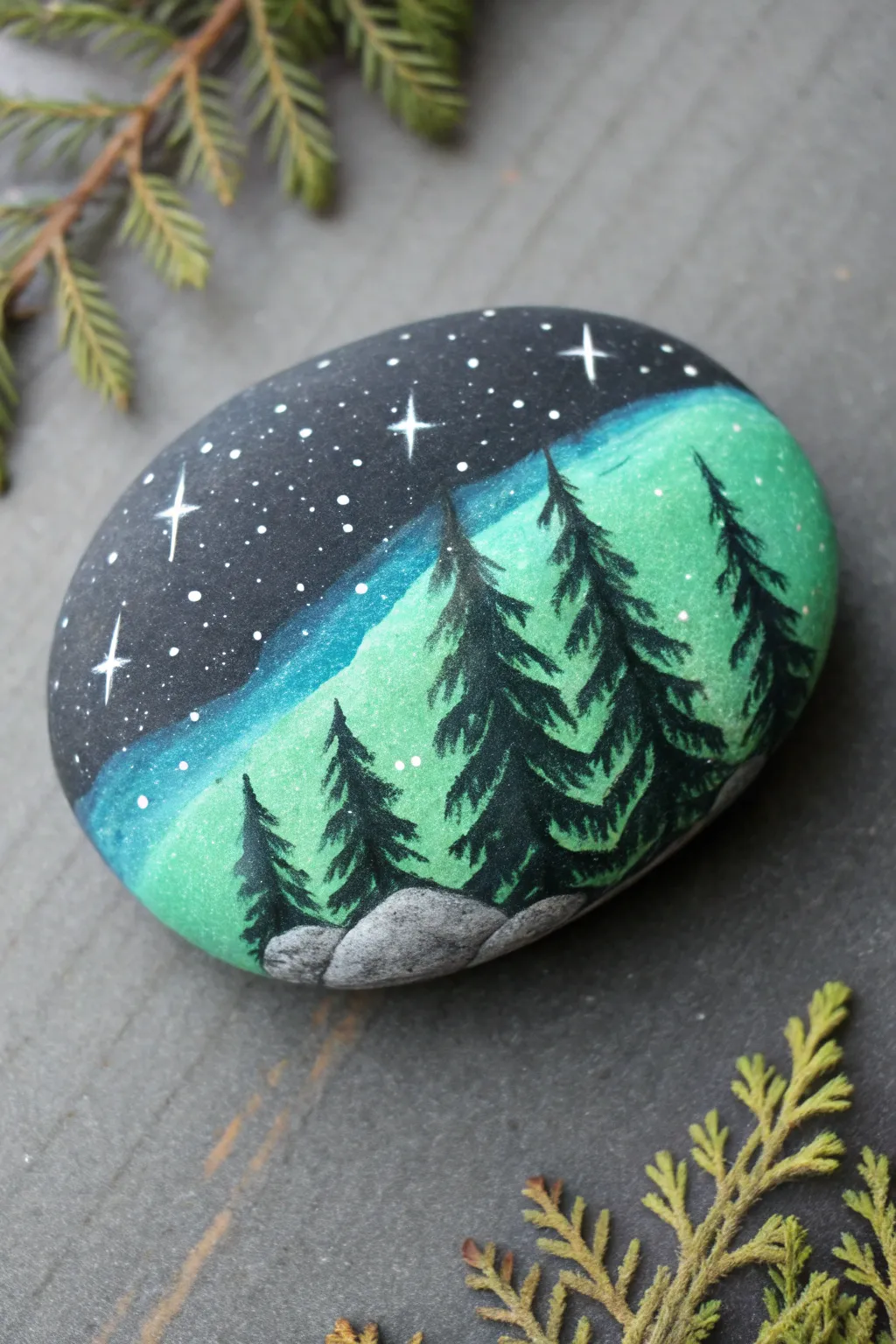Paint a midnight rock with teal aurora ribbons glowing over simple evergreen silhouettes