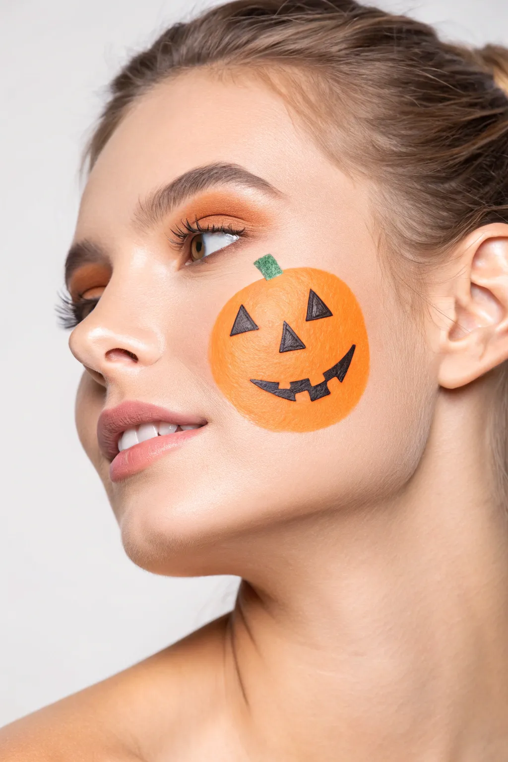 Minimal pumpkin cheek face paint with simple jack o lantern shapes for an easy Halloween look