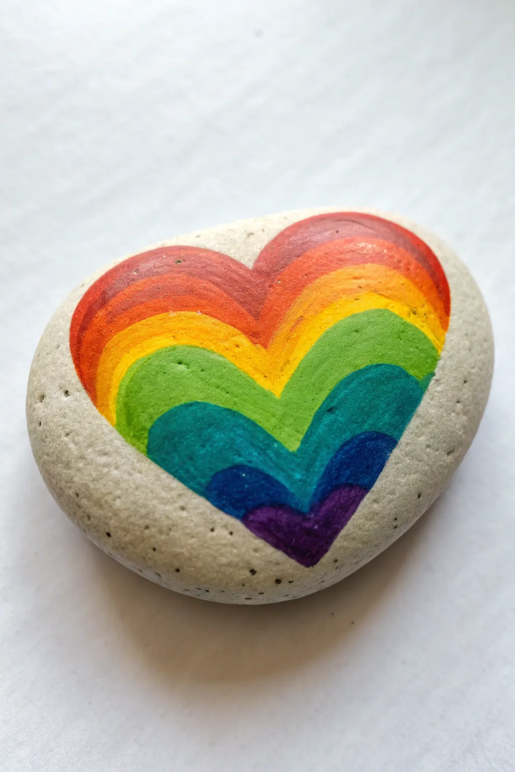 A clean rainbow gradient heart rock on white, minimalist and boho, perfect for love rock painting