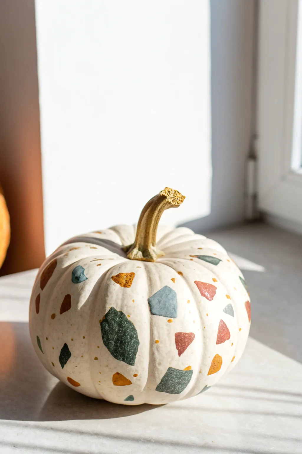 Terrazzo confetti mini pumpkin in soft neutrals with tiny gold accents, minimalist boho vibe.