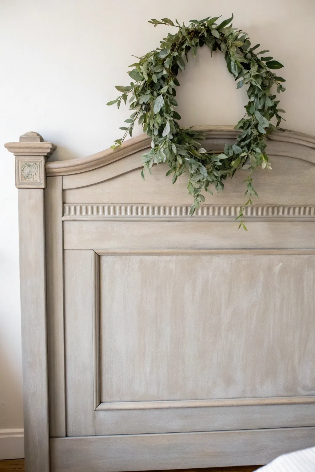 Soft greige chalk-painted headboard with a hand-brushed leafy wreath, calm Scandinavian boho vibe