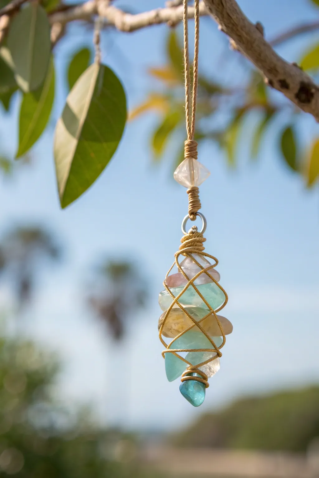 Wire-wrapped glass charm mobile catching sunlight, floating sparkle against soft sky and leaves.
