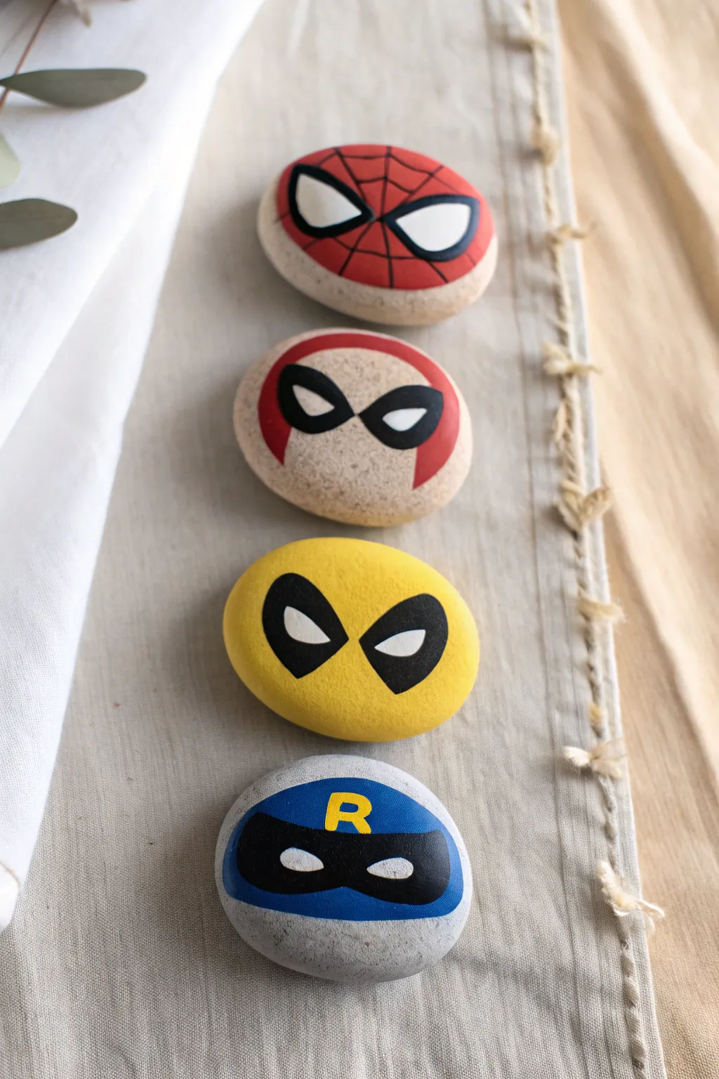 Bold superhero mask story stones in a clean Nordic flat lay, perfect Disney rock painting inspiration