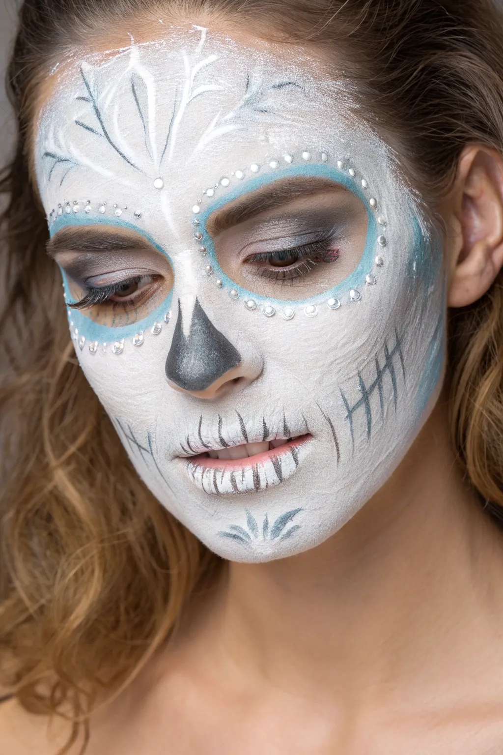 Ice-crystal skull face paint in frosty whites and pale blues, clean winter minimalism.