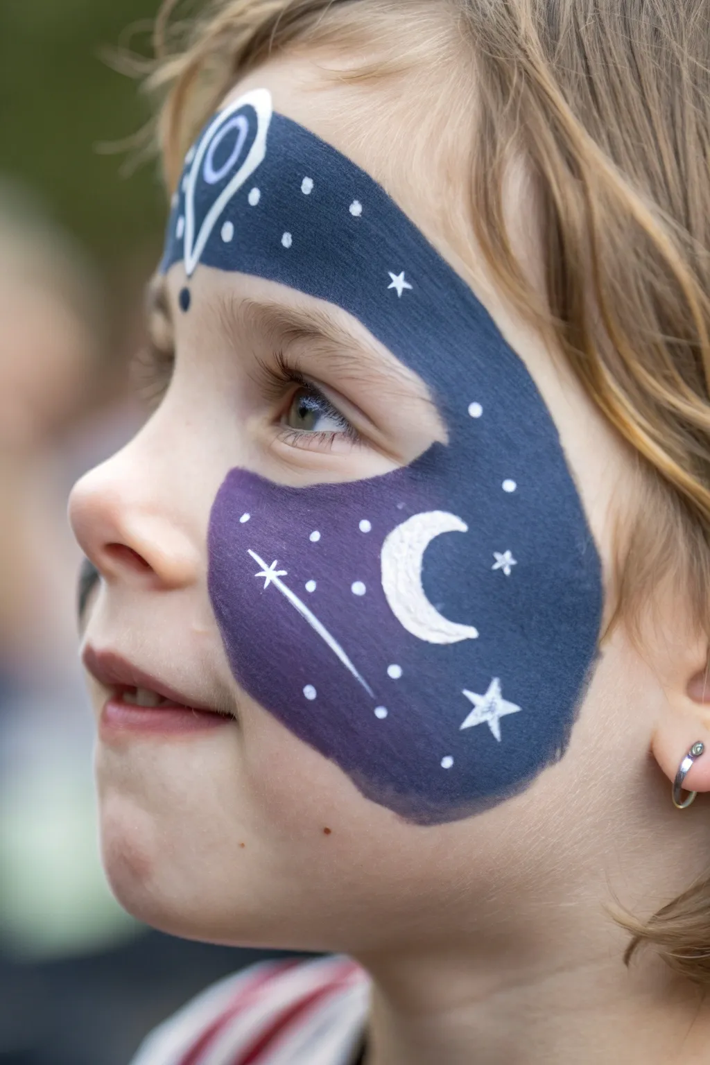 Dreamy space face paint: tiny planet on the cheek and simple star dots across the forehead