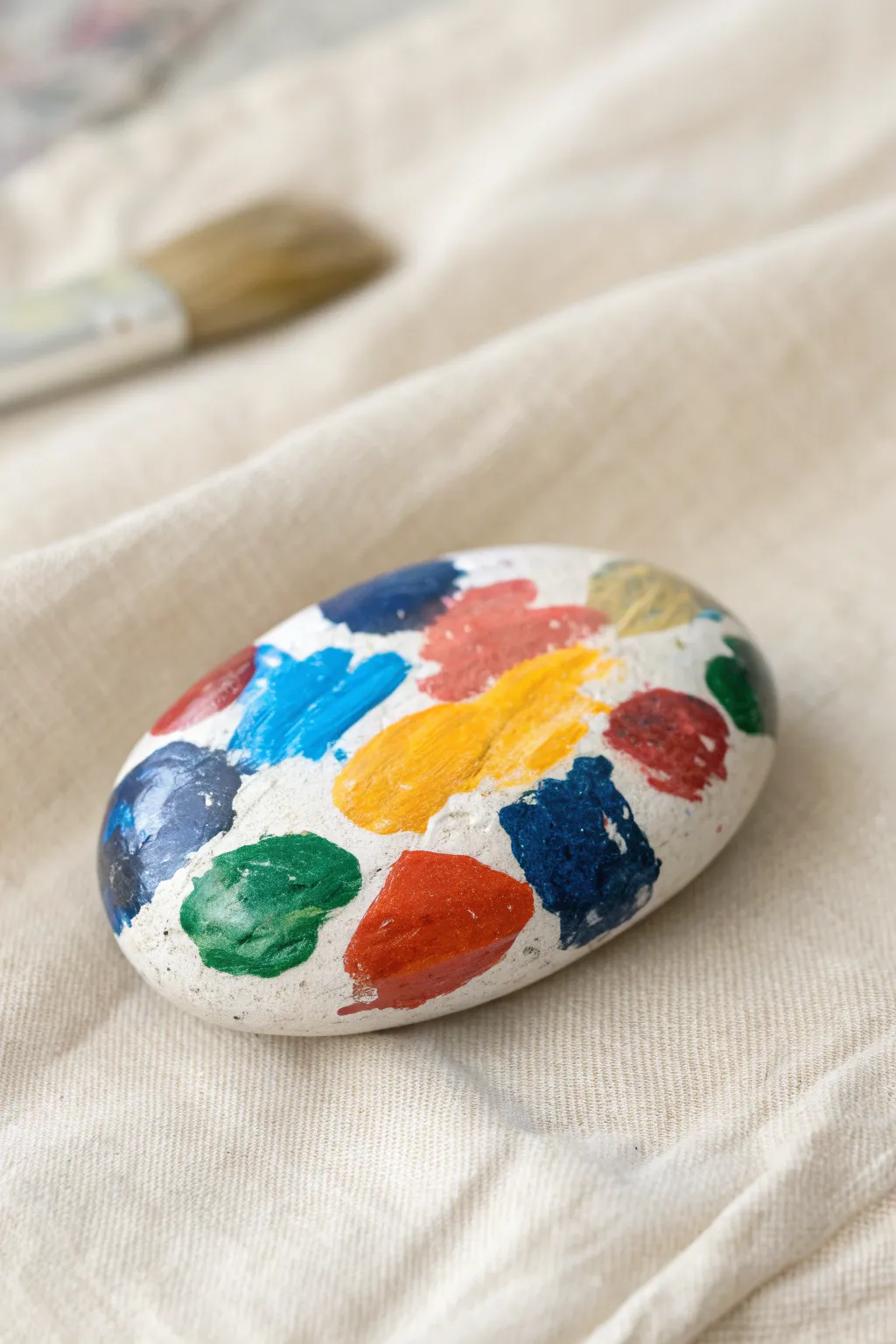 Palette rock with thick, vibrant paint dabs on a calm linen backdrop for chic art room vibes.