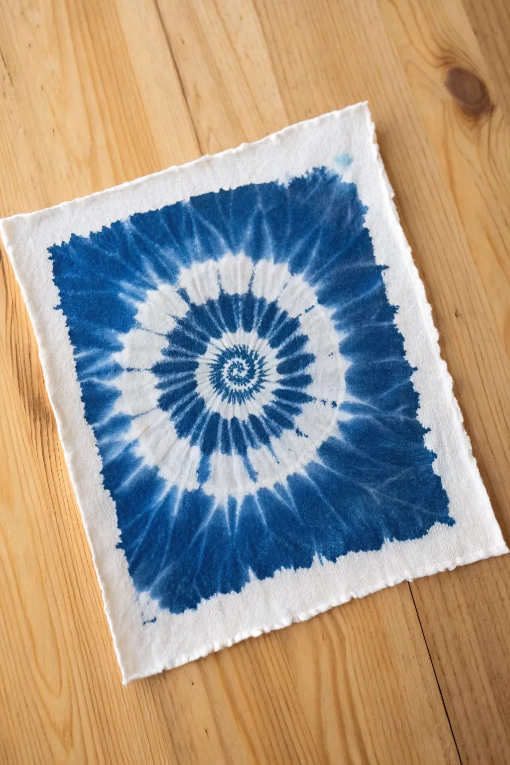 Indigo tie-dye spiral motif in bold blue gradients with crisp highlights on textured watercolor paper.