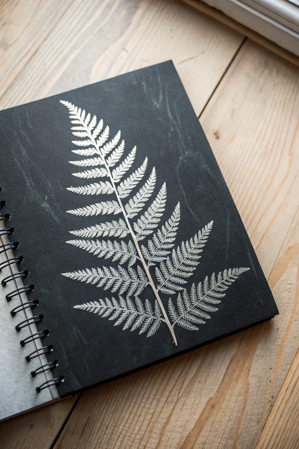 Erase-drawing on a fully shaded graphite page, a bright fern revealed from rich charcoal tones