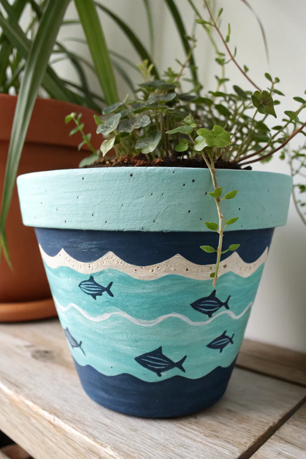 Under-the-sea pot painting with layered waves, fish silhouettes, and a flowing trailing plant