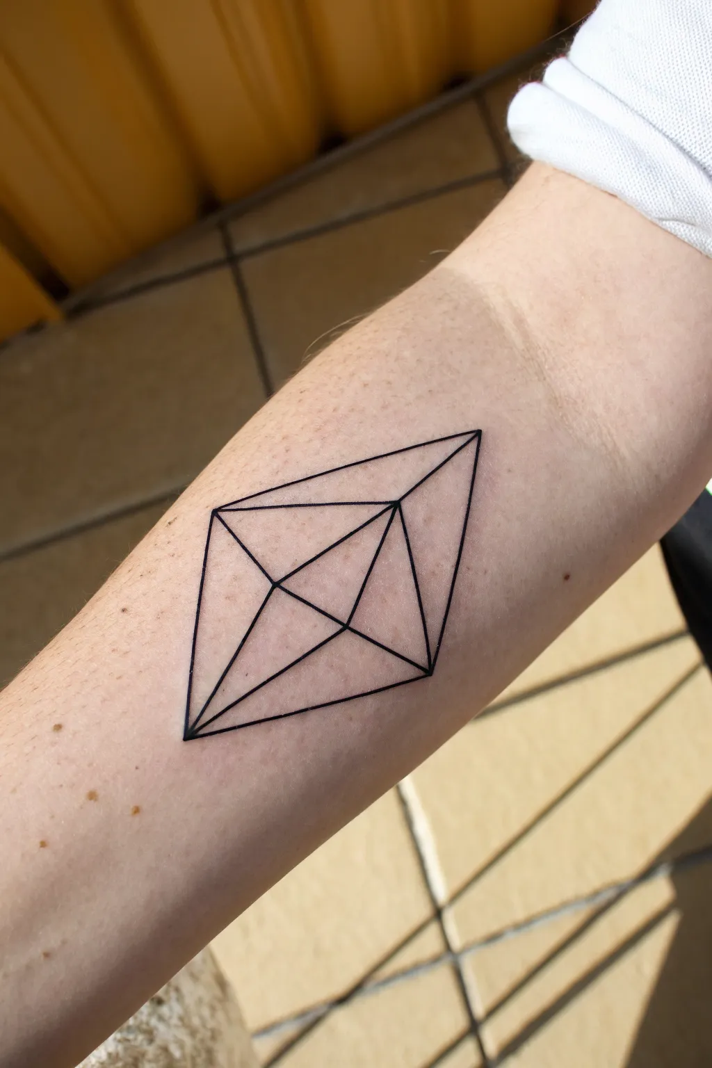 Crisp fine-line triangle diamond tattoo on inner forearm, minimalist and beautifully balanced