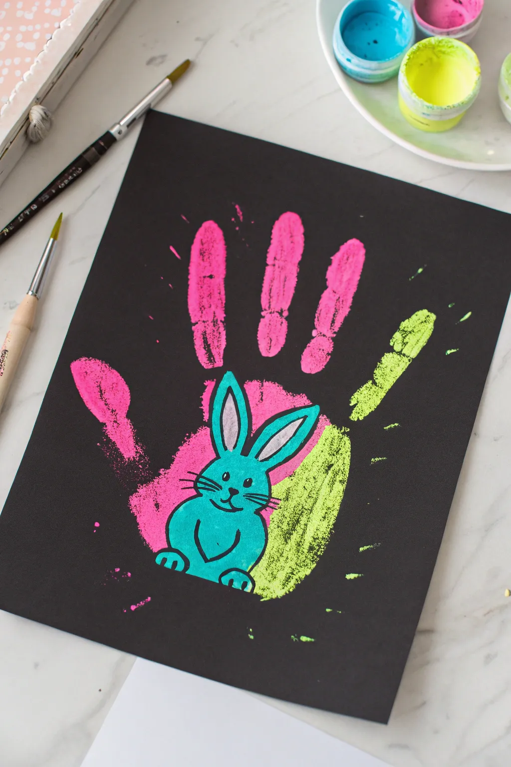 Dramatic neon handprint bunny on matte black paper, a modern Easter craft with glow contrast.