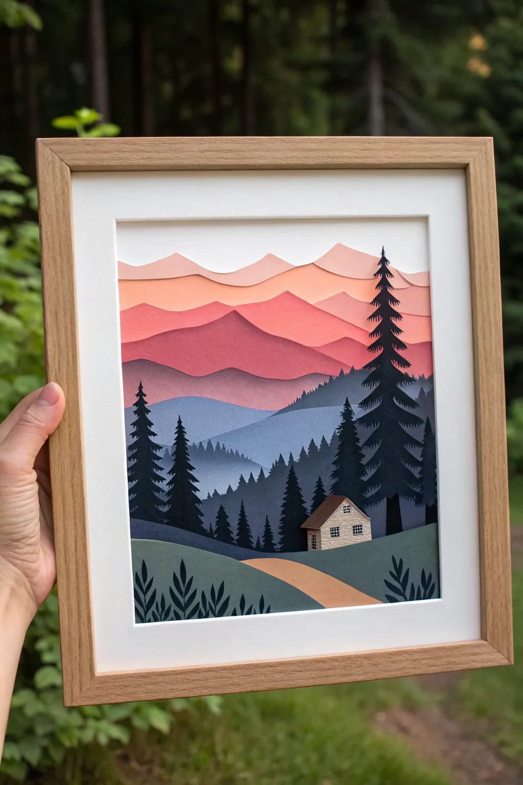 Layered cut-paper sunset silhouettes: hills, pines, and a tiny cabin in bold contrast
