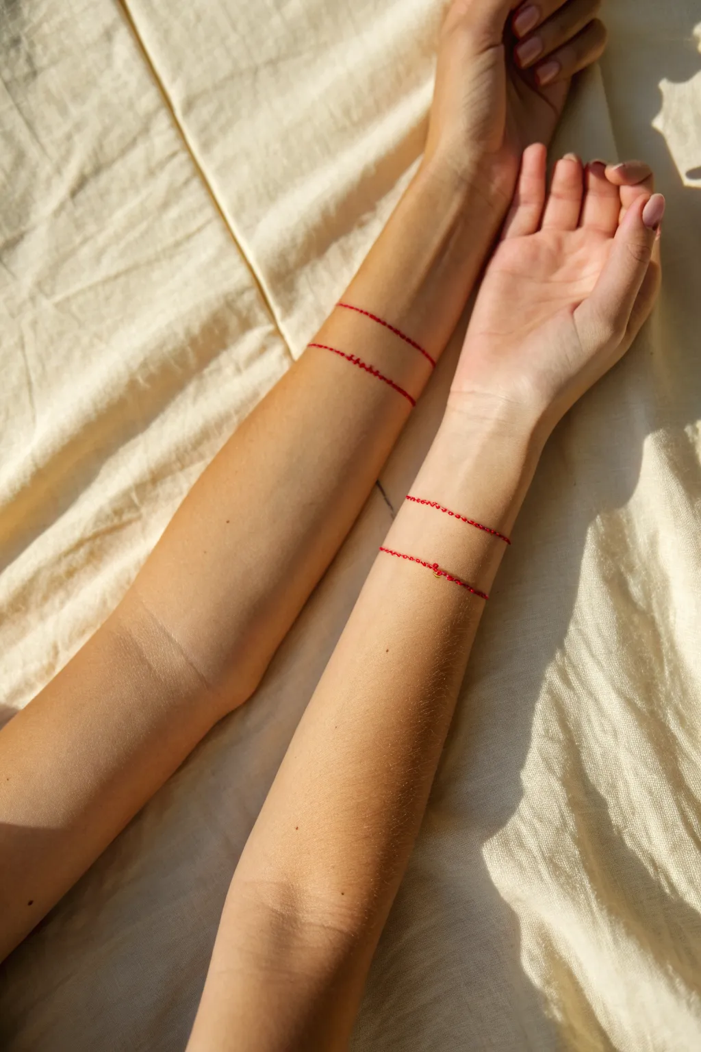 Minimal red string linework tattoos that connect across two arms for a soft love symbol