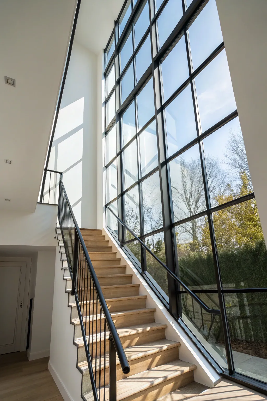 Wraparound stairwell glazing with bold diagonal shadows for a bright, airy vertical statement