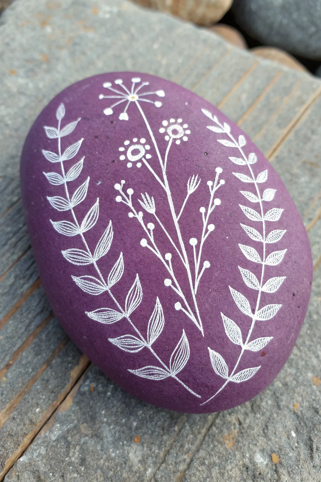 Negative-space purple botanicals: modern rock painting with natural stone leaves and blooms.