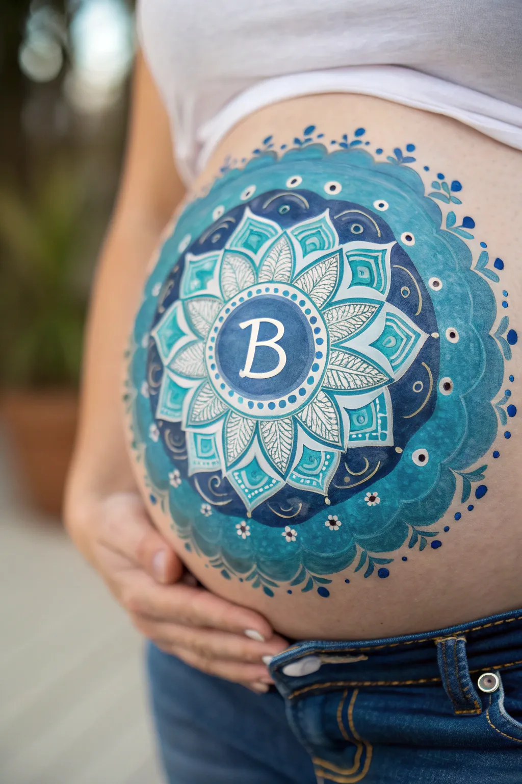 Striking blue mandala belly art with a bold boy initial, minimalist and beautifully crafted.