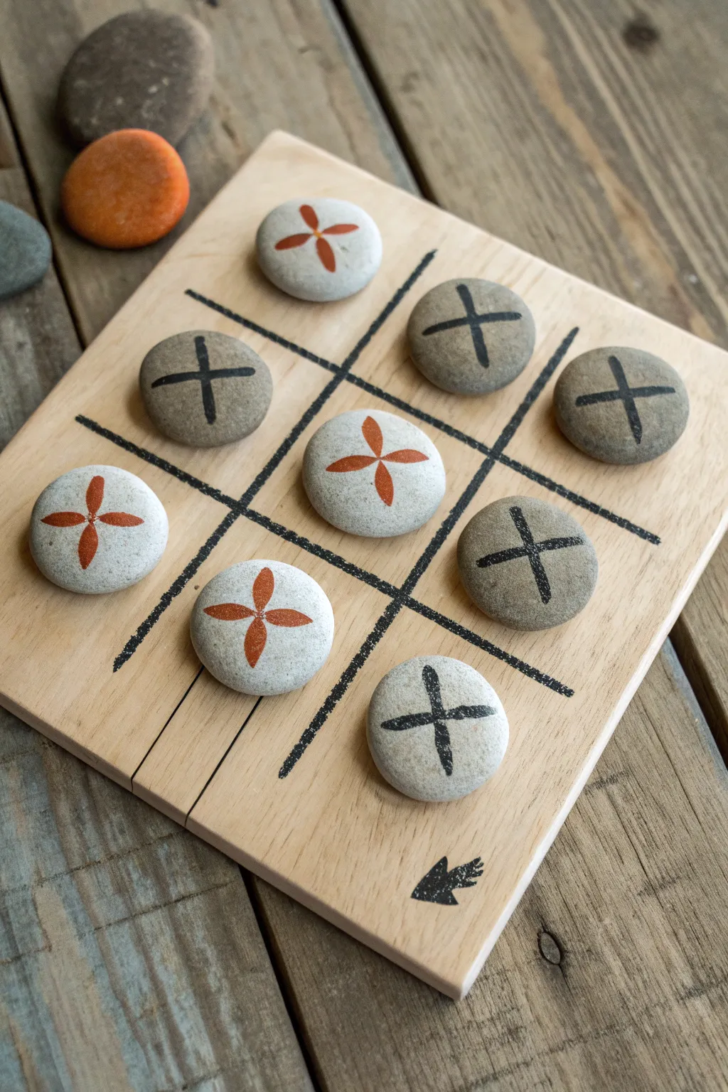 DIY pebble tic-tac-toe set: bold hand-painted symbols on a clean birch grid, ready to play.