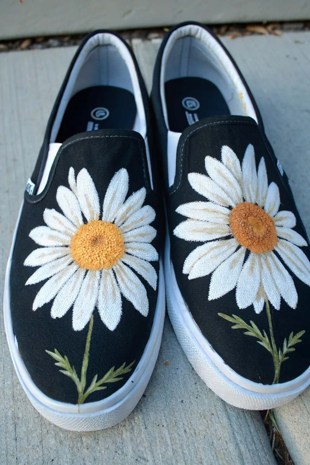Bold white daisies with sunny yellow centers on black shoes, crisp and minimal yet playful