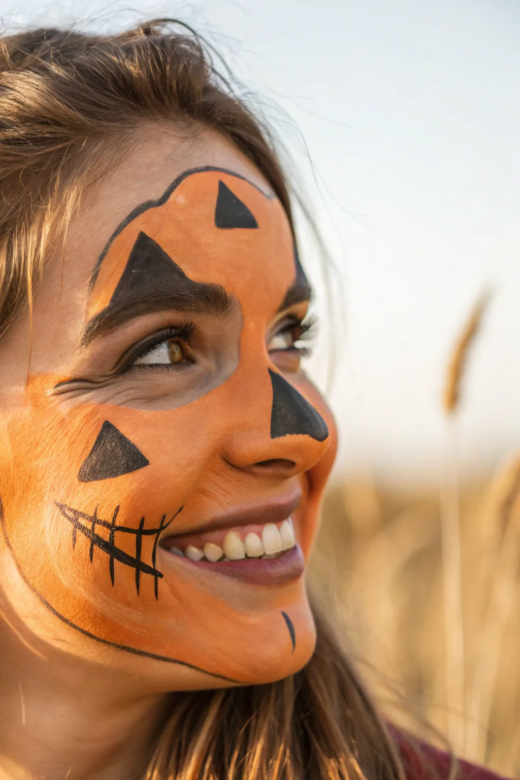 Smiling jack-o-lantern half-mask face paint with warm orange shading and bold black outlines