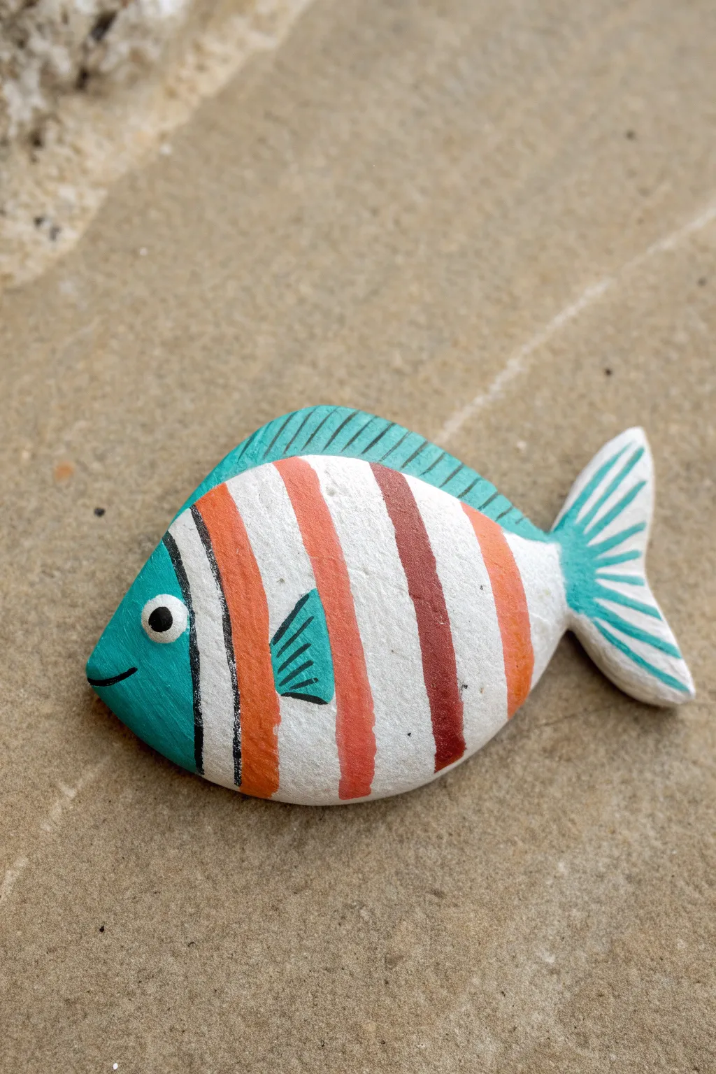 Paint a bold striped tropical fish rock in teal and coral for an easy, modern DIY accent.