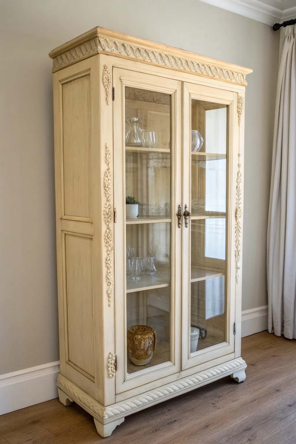 Soft cream curio cabinet with warm antiquing wax, styled with vintage glassware for cozy charm.