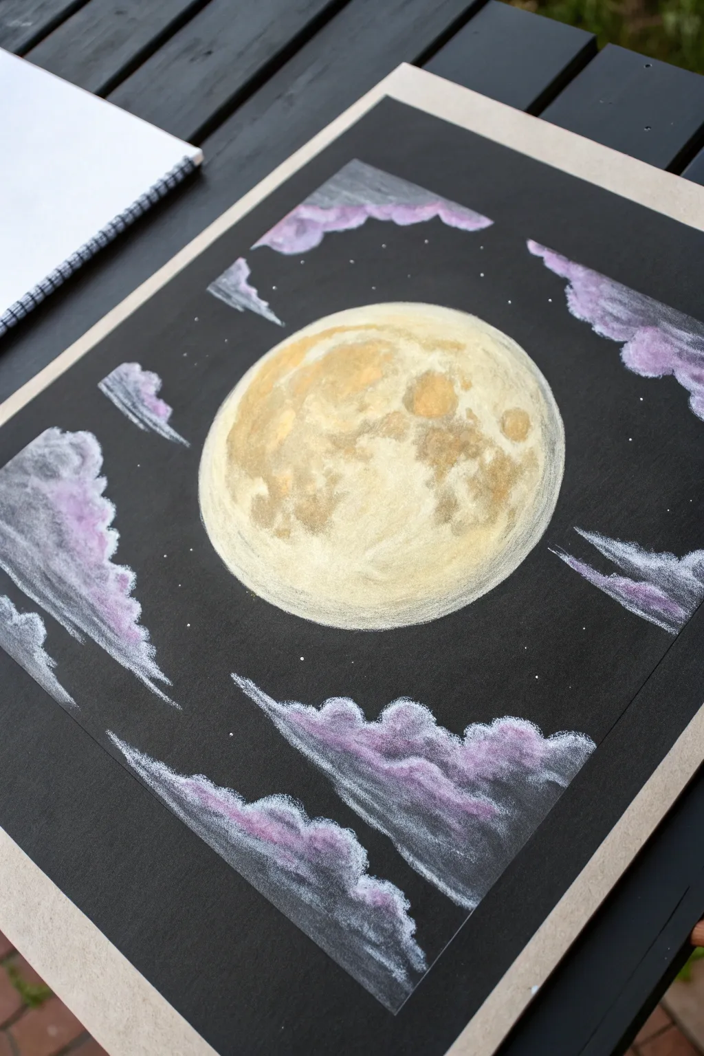 Glowing pastel moon on black paper with soft cloud smudges and crisp luminous highlights