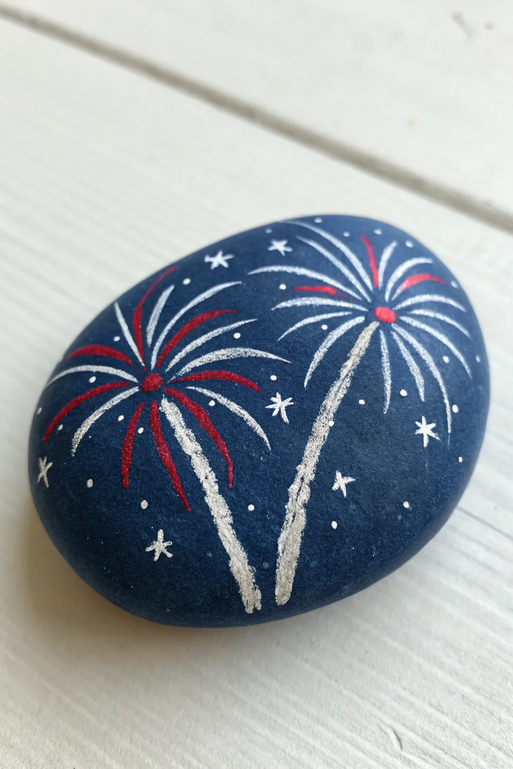 Navy painted rock with glitter-tipped firework bursts for an easy patriotic finale craft.